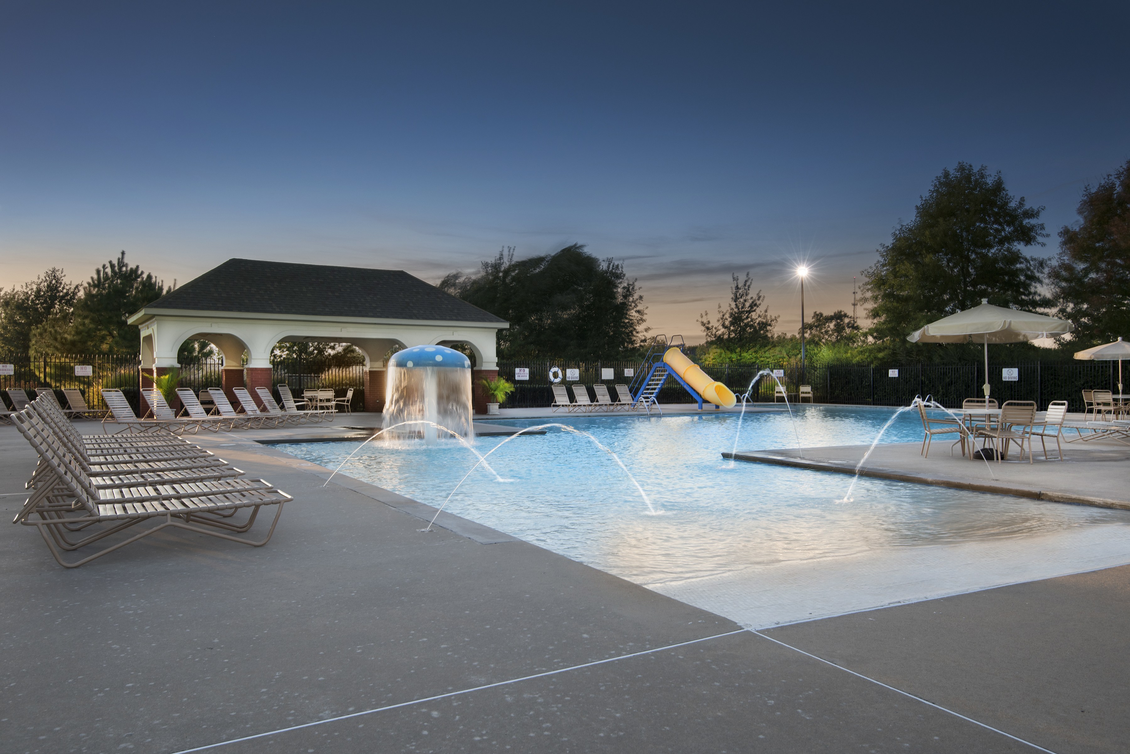 A pool with a waterfall and a slide surrounded by lounge chairs.